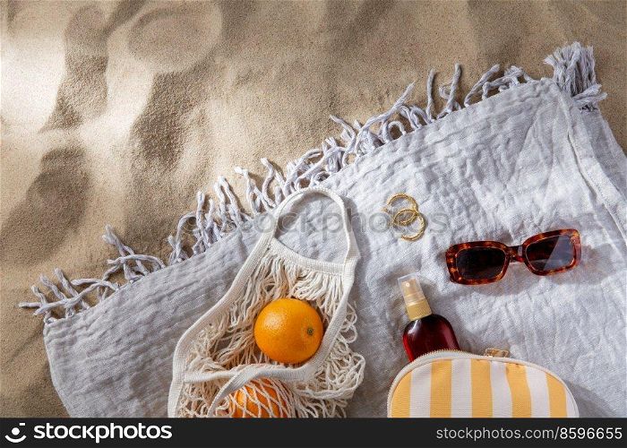 leisure and summer holidays concept - bag of oranges and sunscreen oil on beach blanket. bag of oranges and sunscreen oil on beach blanket