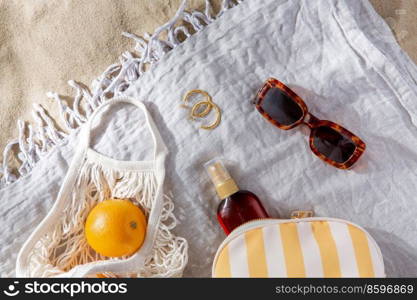 leisure and summer holidays concept - bag of oranges and sunscreen oil on beach blanket. bag of oranges and sunscreen oil on beach blanket