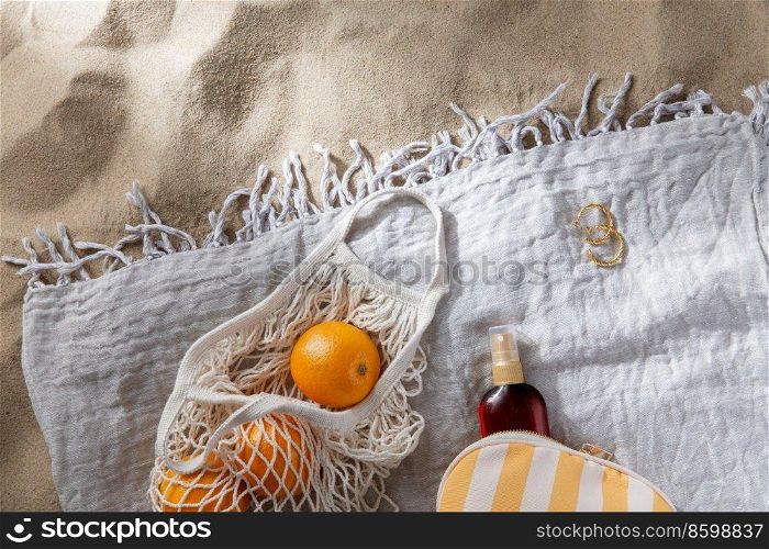 leisure and summer holidays concept - bag of oranges and sunscreen oil on beach blanket. bag of oranges and sunscreen oil on beach blanket