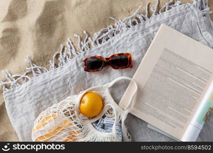 leisure and summer holidays concept - bag of oranges, sunglasses and magazine on blanket on beach sand. bag of oranges, sunglasses and magazine on beach