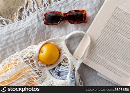 leisure and summer holidays concept - bag of oranges, sunglasses and magazine on blanket on beach sand. bag of oranges, sunglasses and magazine on beach