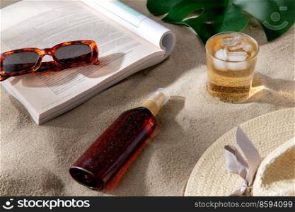 leisure and summer holidays concept - open magazine, sunscreen, glass of ice drink and sunglasses on beach sand. magazine, sunglasses and sunscreen on beach sand