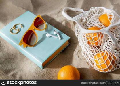 leisure and summer holidays concept - string bag of oranges, earbuds, book and sunglasses on beach sand. bag of oranges, earbuds and sunglasses on beach