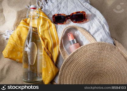 leisure and summer holidays concept - sunscreen in bag, sunglasses, bottle of water, pareo and beach blanket on sand. sunglasses, bag, water bottle, sunscreen on beach