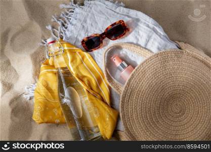 leisure and summer holidays concept - sunscreen in bag, sunglasses, bottle of water, pareo and beach blanket on sand. sunglasses, bag, water bottle, sunscreen on beach