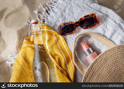 leisure and summer holidays concept - sunscreen in bag, sunglasses, bottle of water, pareo and beach blanket on sand. sunglasses, bag, water bottle, sunscreen on beach