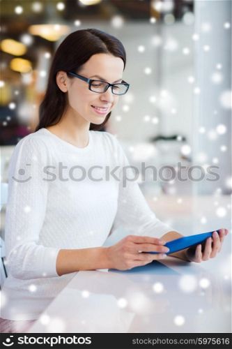 leisure, business, people, technology and lifestyle concept - smiling young woman in eyeglasses with tablet pc computer at cafe over snow effect