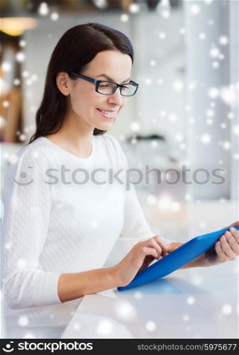 leisure, business, people, technology and lifestyle concept - smiling young woman in eyeglasses with tablet pc computer at cafe over snow effect