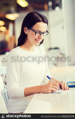 leisure, business, people, technology and lifestyle concept - smiling young woman in eyeglasses with tablet pc computer and notebook taking notes at cafe