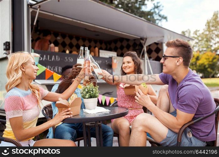 leisure, celebration and people concept - happy friends clinking bottles of non-alcoholic drinks and eating at food truck. friends clinking drinks and eating at food truck