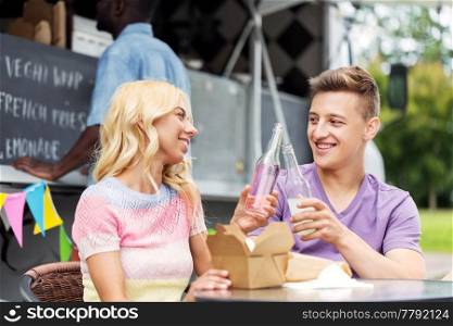 leisure, celebration and people concept - happy friends clinking bottles of non-alcoholic drinks and eating wok at food truck. friends clinking drinks and eating at food truck