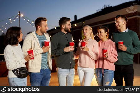 leisure, celebration and people concept - happy friends with drinks at rooftop party at night. friends with drinks at rooftop party