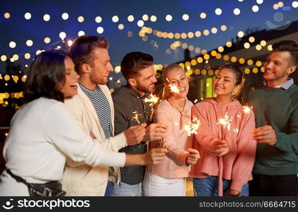 leisure, celebration and people concept - happy friends with sparklers at rooftop party at night with blurred bokeh lights. happy friends with sparklers at rooftop party