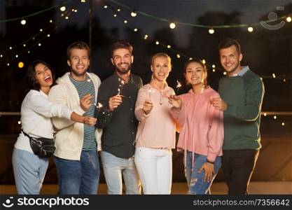 leisure, celebration and people concept - happy friends with sparklers at rooftop party at night. happy friends with sparklers at rooftop party
