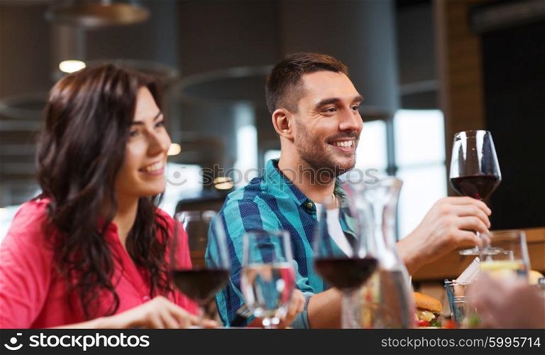 leisure, celebration, food and drinks, people and holidays concept - happy couple and friends clinking glasses of wine at restaurant