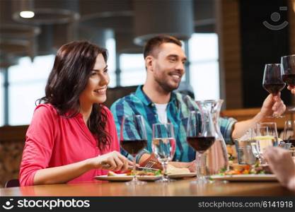 leisure, celebration, food and drinks, people and holidays concept - happy couple and friends clinking glasses of wine at restaurant