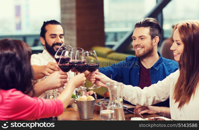 leisure, celebration, food and drinks, people and holidays concept - smiling friends having dinner and drinking red wine at restaurant. friends dining and drinking wine at restaurant