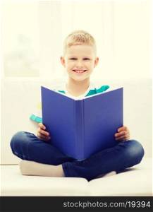 leisure, childhood, education and home concept - smiling little boy reading book and sitting on couch at home