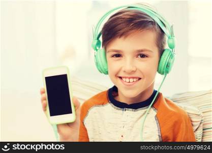 leisure, children, technology, advertisement and people concept - smiling boy with smartphone and headphones listening to music at home. happy boy with smartphone and headphones at home
