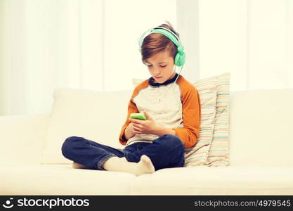 leisure, children, technology and people concept - boy with smartphone and headphones listening to music or playing game at home. boy with smartphone and headphones at home