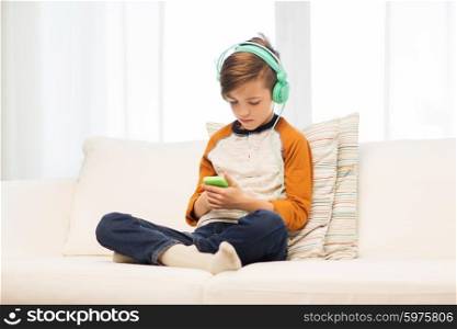 leisure, children, technology and people concept - boy with smartphone and headphones listening to music or playing game at home