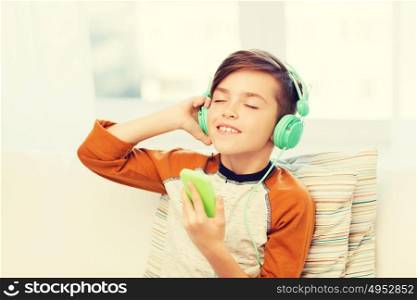 leisure, children, technology and people concept - smiling boy with smartphone and headphones listening to music at home. happy boy with smartphone and headphones at home