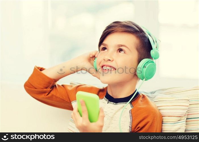 leisure, children, technology and people concept - smiling boy with smartphone and headphones listening to music at home. happy boy with smartphone and headphones at home