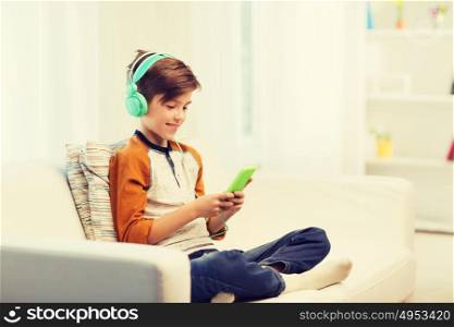 leisure, children, technology and people concept - smiling boy with smartphone and headphones listening to music or playing game at home. happy boy with smartphone and headphones at home