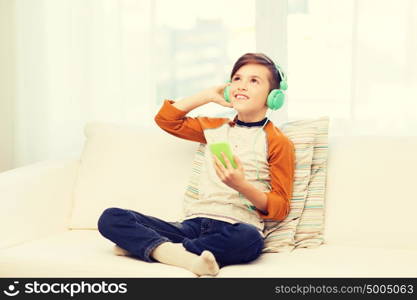 leisure, children, technology and people concept - smiling boy with smartphone and headphones listening to music at home. happy boy with smartphone and headphones at home