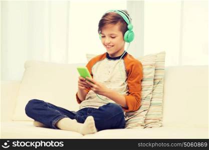 leisure, children, technology and people concept - smiling boy with smartphone and headphones listening to music or playing game at home. happy boy with smartphone and headphones at home