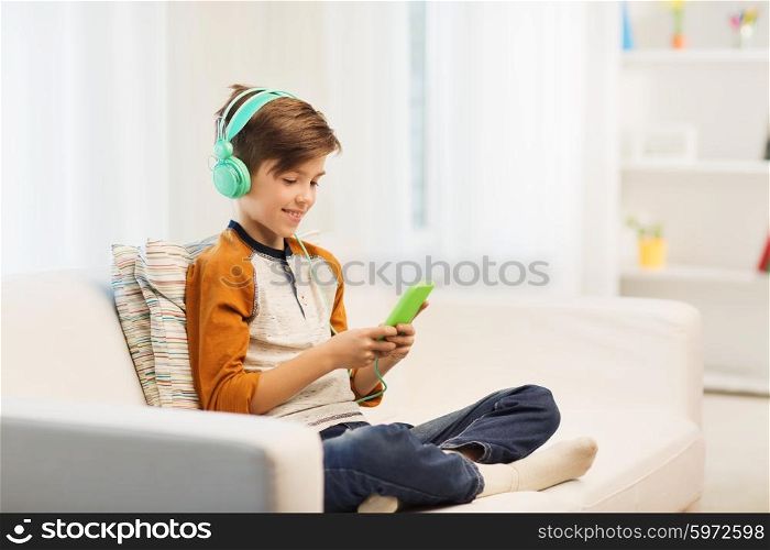 leisure, children, technology and people concept - smiling boy with smartphone and headphones listening to music or playing game at home