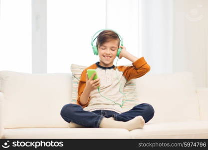 leisure, children, technology and people concept - smiling boy with smartphone and headphones listening to music at home