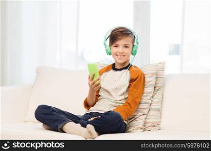 leisure, children, technology and people concept - smiling boy with smartphone and headphones listening to music at home