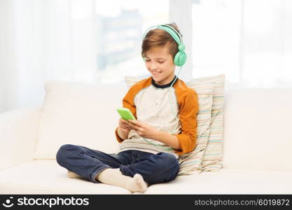 leisure, children, technology and people concept - smiling boy with smartphone and headphones listening to music or playing game at home