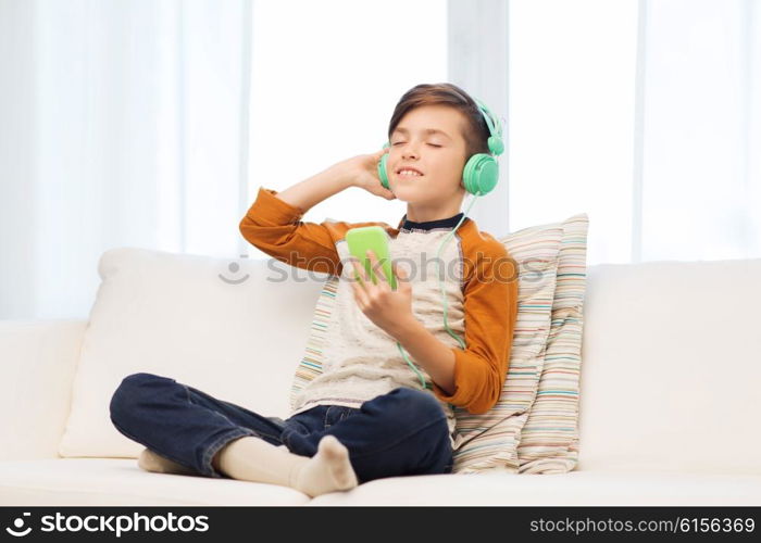 leisure, children, technology and people concept - smiling boy with smartphone and headphones listening to music at home