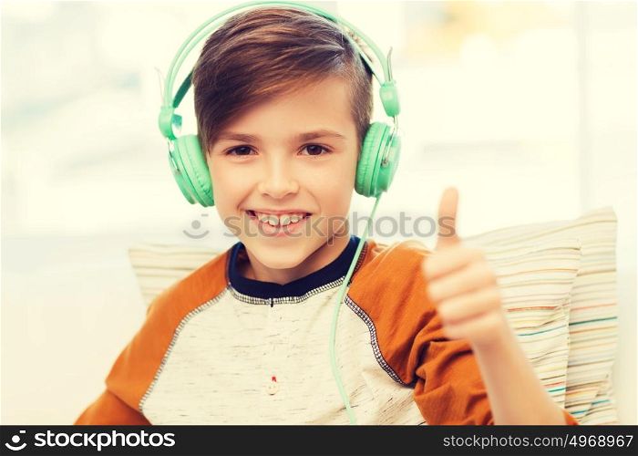 leisure, children, technology, gesture and people concept - smiling boy with headphones listening to music and showing thumbs up at home. happy boy in headphones showing thumbs up at home