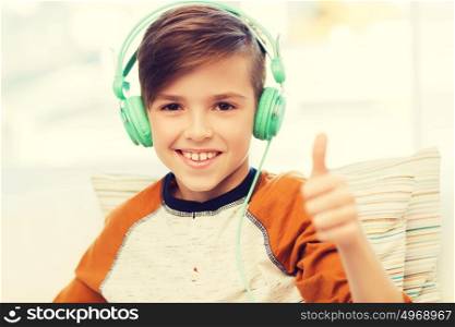 leisure, children, technology, gesture and people concept - smiling boy with headphones listening to music and showing thumbs up at home. happy boy in headphones showing thumbs up at home