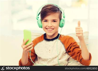 leisure, children, technology, gesture and people concept - smiling boy with smartphone and headphones listening to music and showing thumbs up at home. happy boy with smartphone and headphones at home