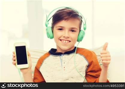 leisure, children, technology, gesture and people concept - smiling boy with smartphone and headphones listening to music and showing thumbs up at home. happy boy with smartphone and headphones at home