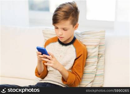 leisure, children, technology, internet communication and people concept - boy with smartphone texting message or playing game at home