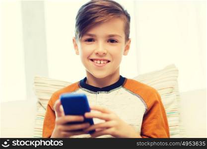 leisure, children, technology, internet communication and people concept - smiling boy with smartphone texting message or playing game at home. boy with smartphone texting or playing at home