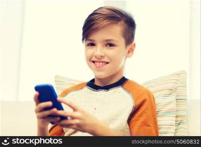 leisure, children, technology, internet communication and people concept - smiling boy with smartphone texting message or playing game at home. boy with smartphone texting or playing at home