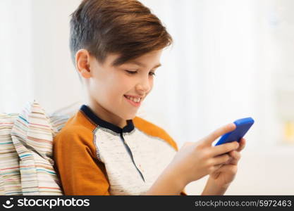 leisure, children, technology, internet communication and people concept - smiling boy with smartphone texting message or playing game at home