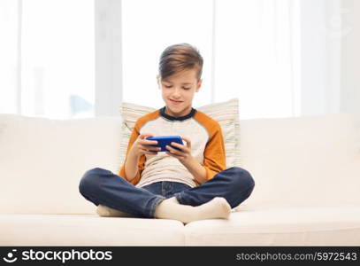 leisure, children, technology, internet communication and people concept - smiling boy with smartphone texting message or playing game at home