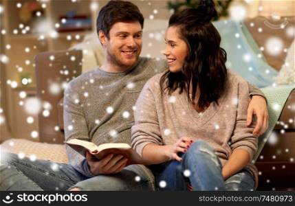 leisure, christmas and people concept - happy couple reading book at home over snow. happy couple reading book at home