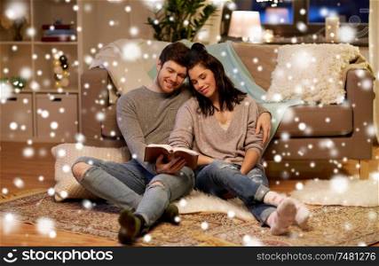leisure, christmas and people concept - happy couple reading book at home over snow. happy couple reading book at home