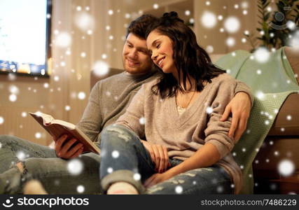 leisure, christmas and people concept - happy couple reading book at home over snow. happy couple reading book at home