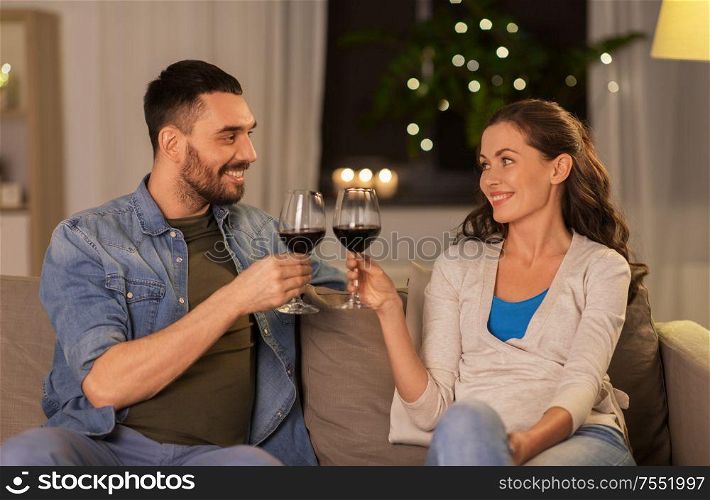 leisure, clebration and valentines day concept - happy couple drinking red wine at home in evening. happy couple drinking red wine at home in evening