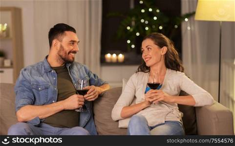 leisure, clebration and valentines day concept - happy couple drinking red wine at home in evening. happy couple drinking red wine at home in evening