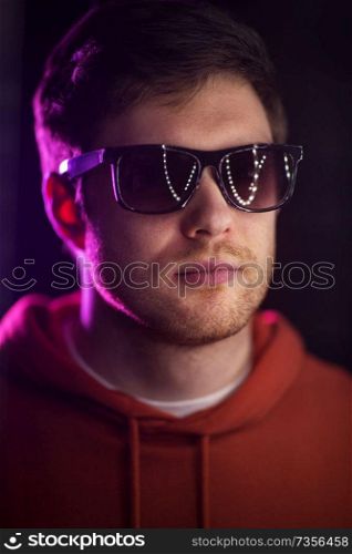 leisure, clubbing and nightlife concept - portrait of smiling young man in sunglasses at dark room over ultra violet neon lights of night club. man in sunglasses over ultra violet neon lights